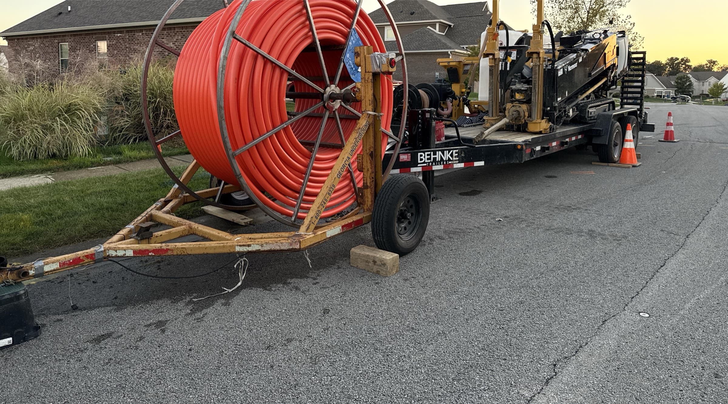 Orange conduit reel and a Vermeer directional drill on a trailer, parked on a residential street in Indianapolis at dusk